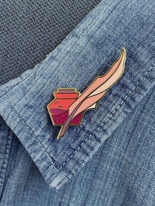 Enamel pin featuring a quill and ink design by Naomi VanDoren, perfect for writers and art enthusiasts.