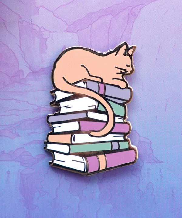 Enamel pin featuring a cute cat sitting on books, designed by Naomi VanDoren for Adventure Art & Stories.