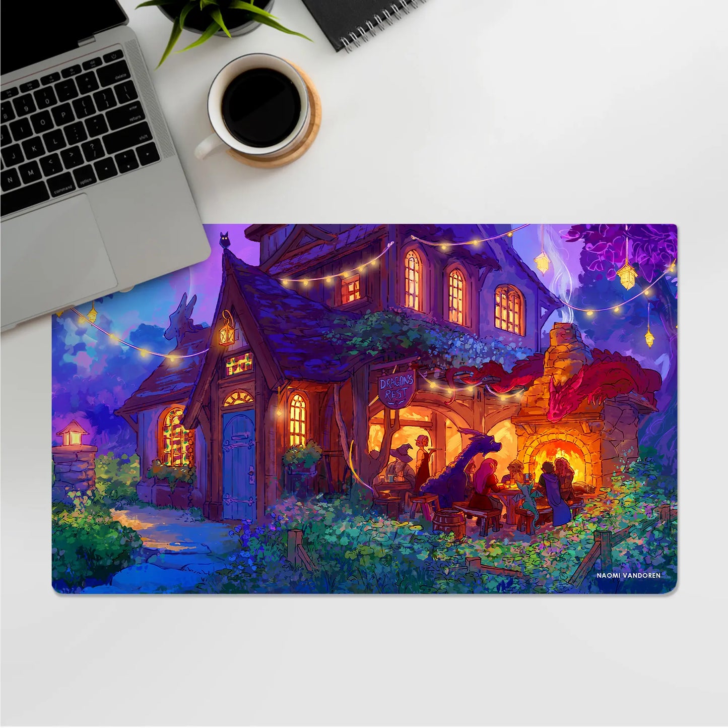 Colorful placemat with a fairy tale scene of a house and characters, placed on a desk with a laptop and coffee.