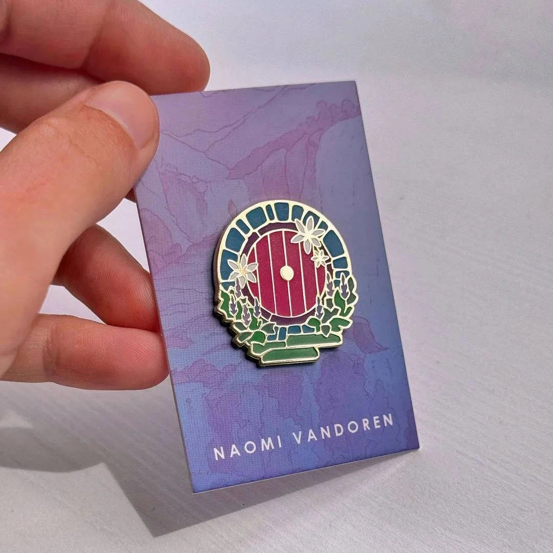 Red Hobbit door enamel pin by Naomi VanDoren featuring detailed hobbit door design for adventure-themed accessories.