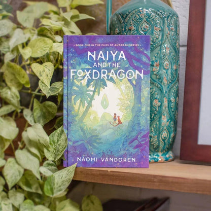 Illustrated novel "Naiya and the Foxdragon" by Naomi VanDoren displayed on a shelf, featuring colorful cover art and fantasy theme.