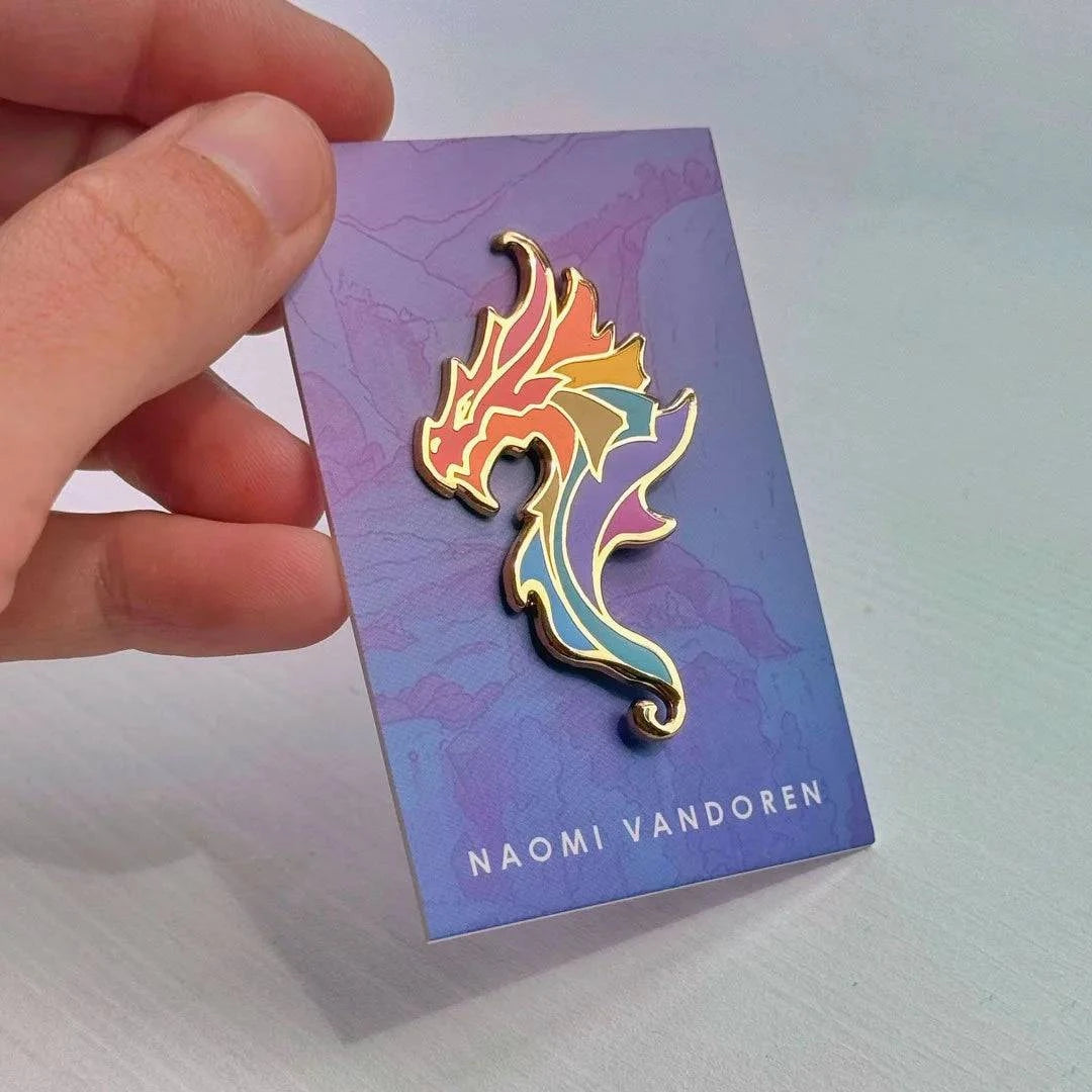 Colorful Rainbow Dragon enamel pin by Naomi VanDoren featuring a vibrant, detailed dragon design on a metal backing.
